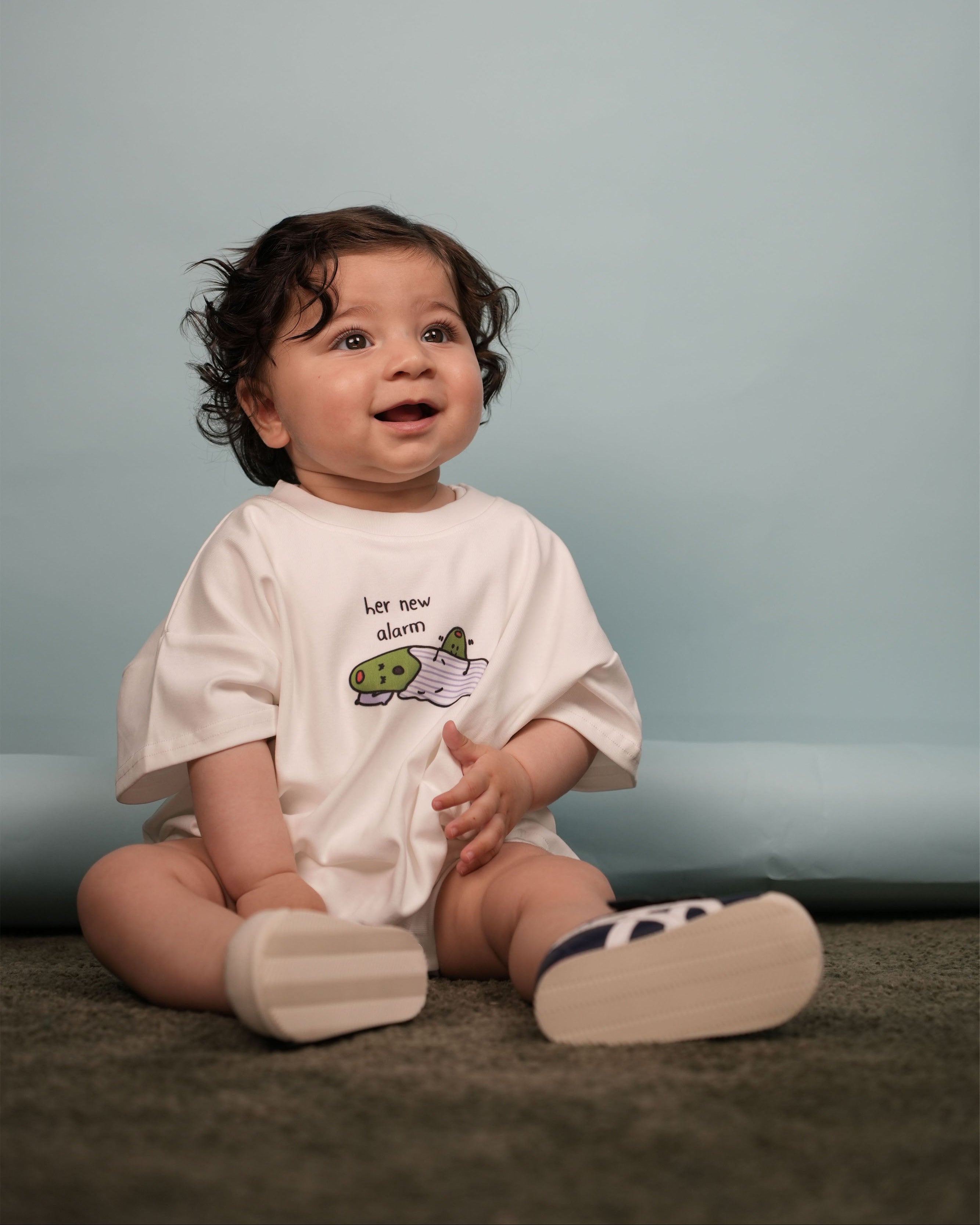 Lifestyle shot of a newborn in the snow white "Her New Alarm" romper in a bright nursery.