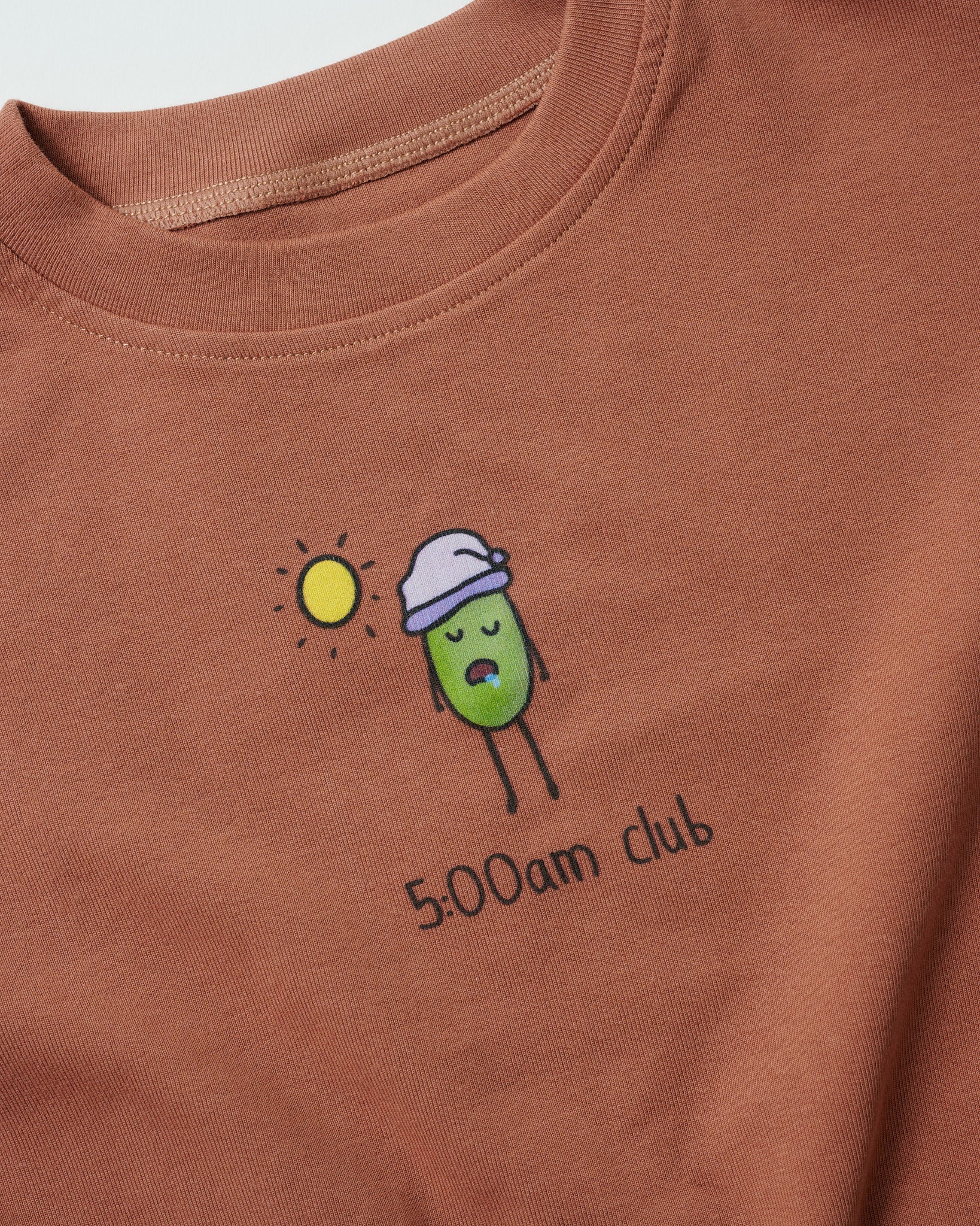 Detailed shot of "5:00am Club" digital print design on terracotta clay babywear.