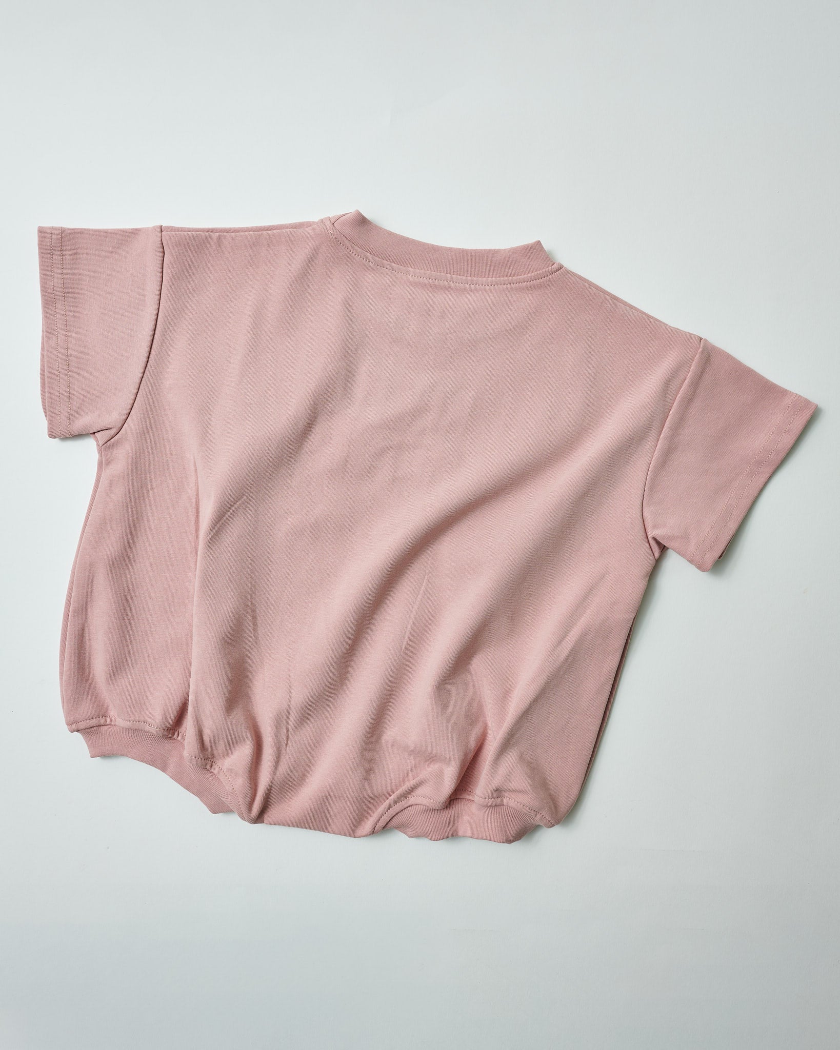 Back view of oversized blush pink toddler romper showing the relaxed minimalist fit.