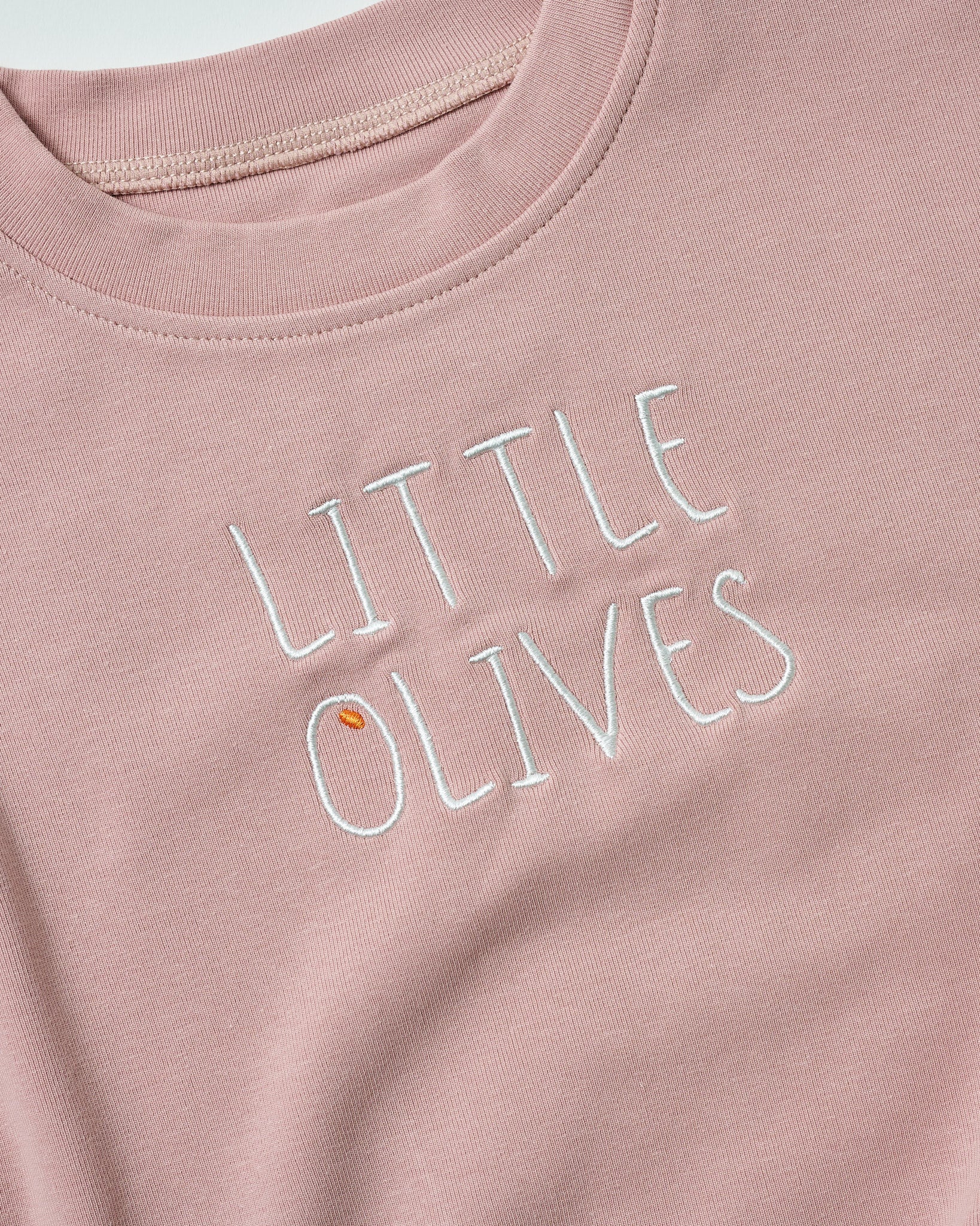 Detailed shot of white "LITTLE OLIVES" embroidery on soft blush pink organic fabric.