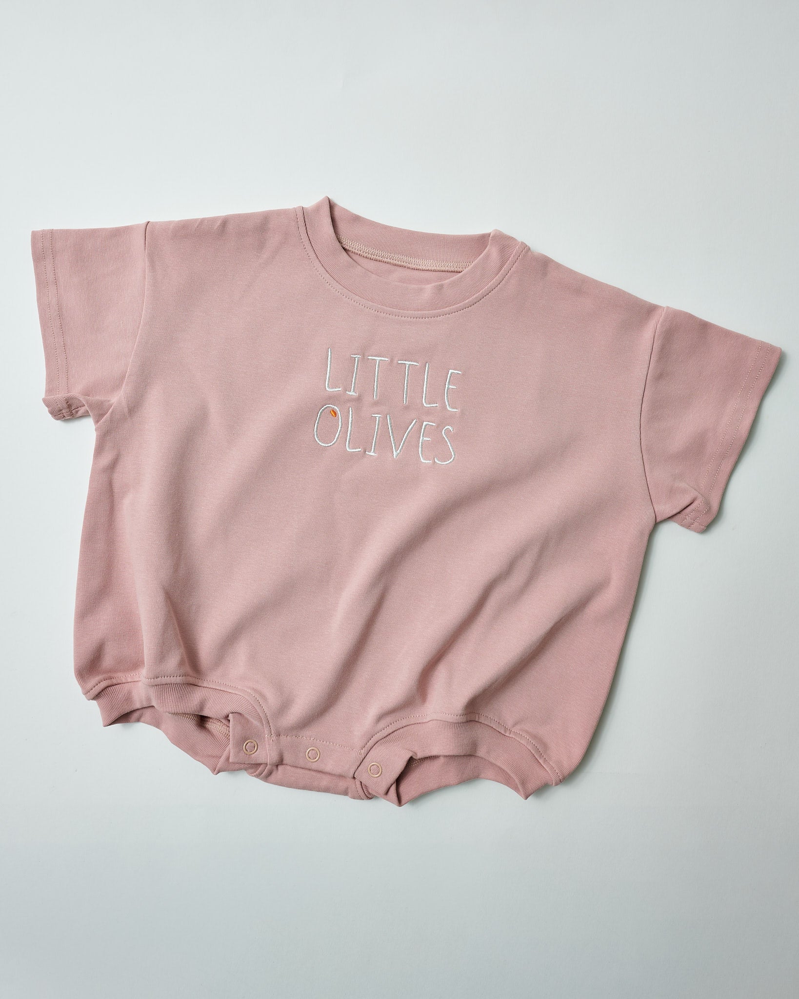 Front view of Little Olives white embroidered baby romper in blush pink organic cotton.