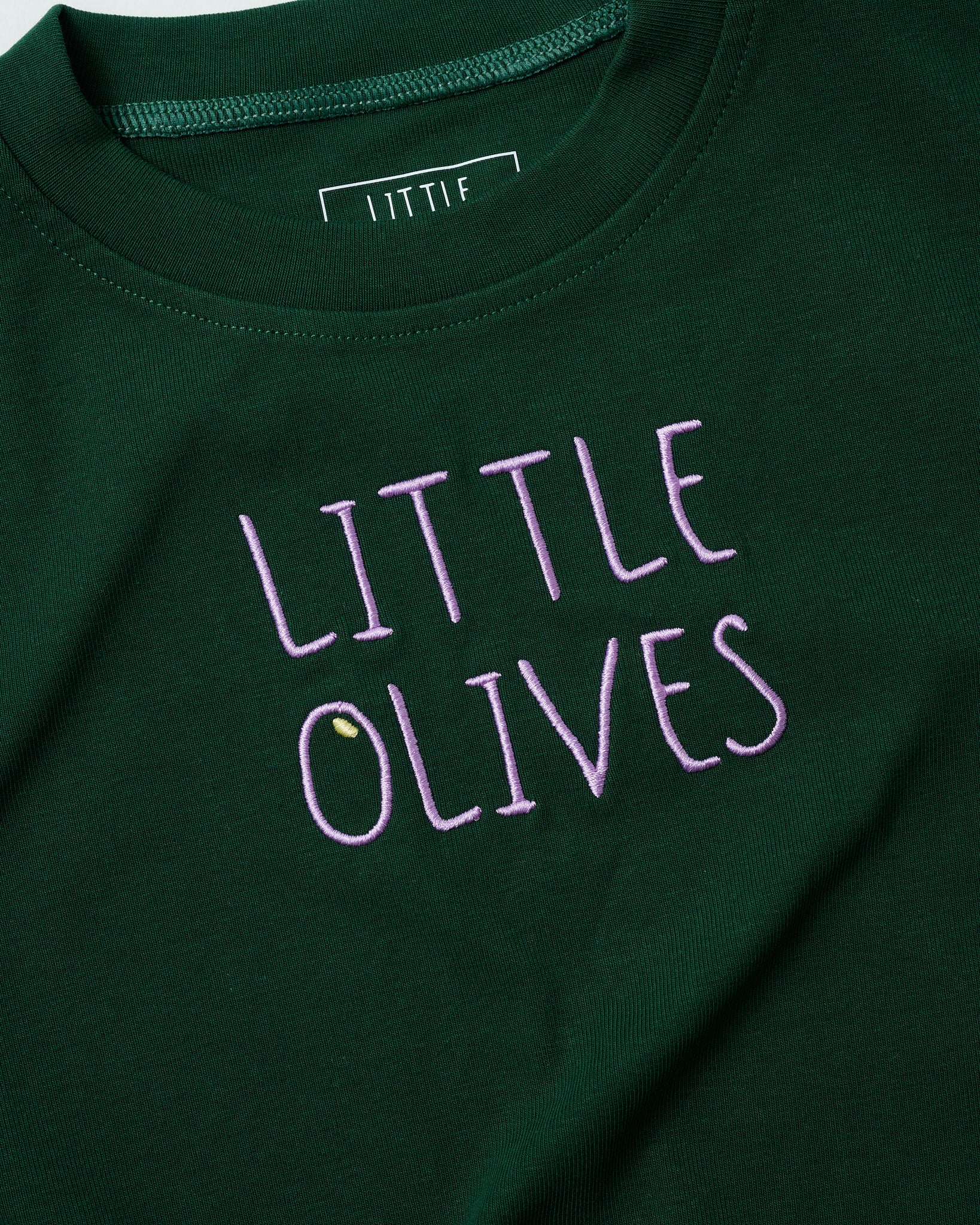 Detailed shot of light purple "LITTLE OLIVES" embroidery on forest green organic cotton.