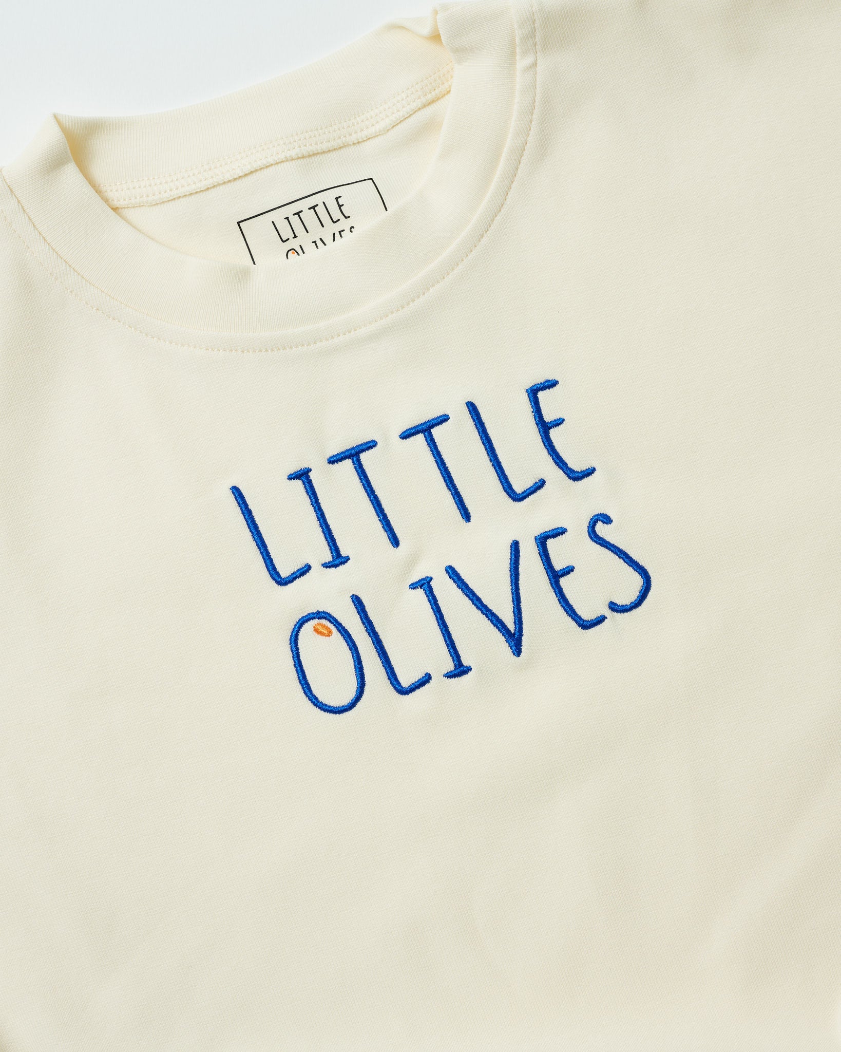 Close-up of navy blue 'Little Olives' embroidery on a natural cream organic cotton baby romper.