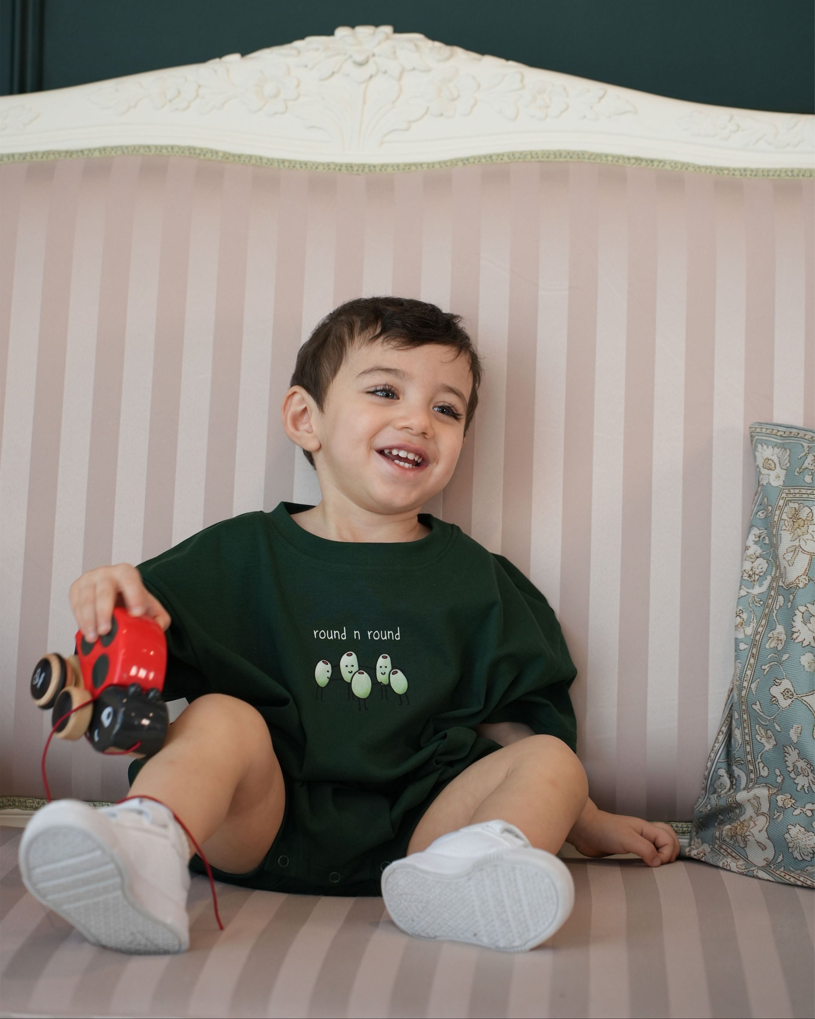 Lifestyle shot of a toddler playing in the forest green Round n Round romper.