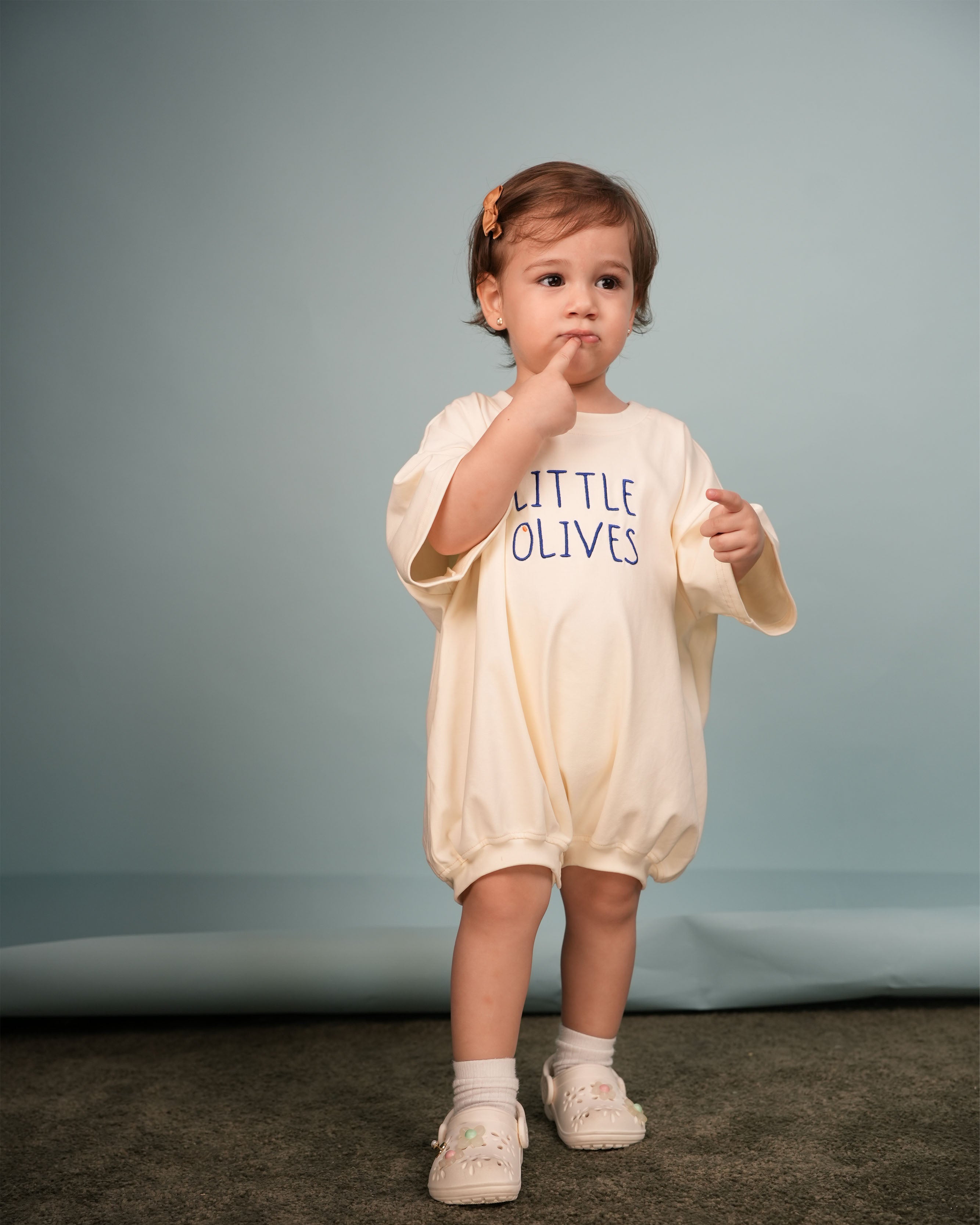 lifestyle shot of a baby wearing the oversized embroidered cream romper in a modern nursery.